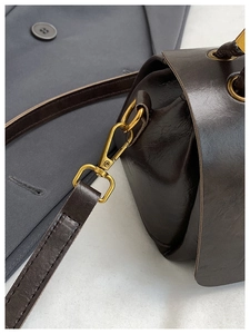 Detail view of vintage gold lobster clasp and dark brown leather stitching on a small bag