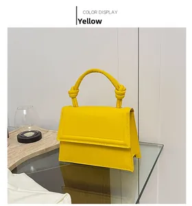 Detail of yellow crossbody bag featuring a unique knotted handle and structured trapezoid shape