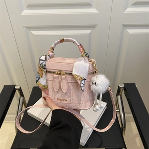 Close-up of pink textured leather bag with floral scarf handle and plush monster charm