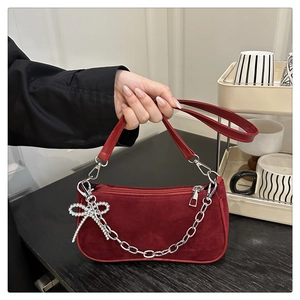 Detail of dark red suede shoulder bag with silver chain and rhinestone bow charm