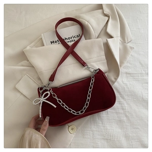 Détail d'un sac bandoulière en velours rouge avec chaîne argentée et nœud en perles sur blazer