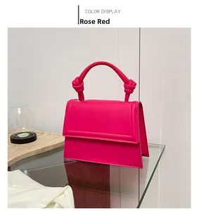 Detailed view of rose red leather handbag with unique knotted handle and flap closure