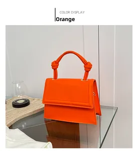 Detail of minimalist orange leather handbag with stylish knotted handle and magnetic flap