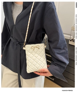 White quilted crossbody bag with bow detail and chain strap shown on model shoulder