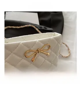 Detail of white quilted mini bag featuring golden bow buckle and chain strap