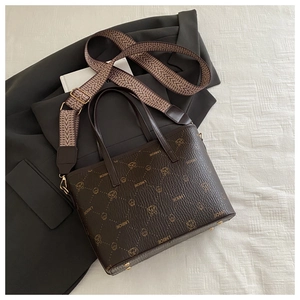 Détail d'un sac seau marron en cuir avec logo imprimé et large bandoulière tissée