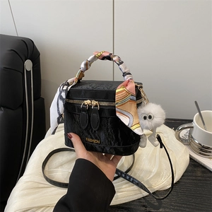 Close-up of black patent leather square bag with silk scarf handle and plush charm