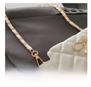 Close-up of white quilted crossbody bag with gold metal chain and bow clasp detail