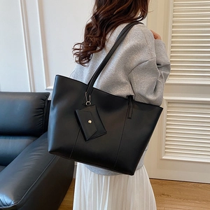 Large black leather tote bag with small coin purse shown on model in modern interior