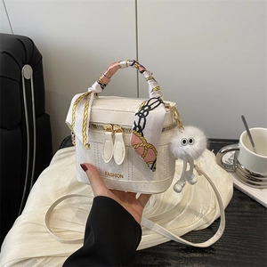 Close-up of white boxy handbag with silk scarf handle and plush pendant accessory