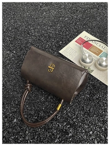 Detail of dark brown cylinder bag showing leather texture and gold geometric buckle