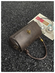 Close-up of a retro dark brown cylindrical handbag with golden twist lock on black gravel