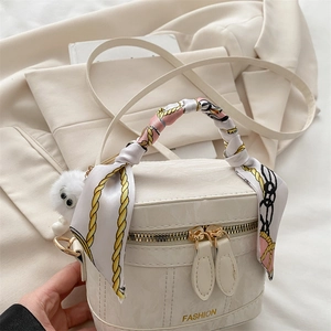 Detail of white cylindrical handbag with silk scarf handle and plush ball on beige suit