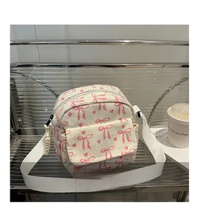 Détail macro du sac bandoulière en velours côtelé beige avec motifs nœuds et cœurs