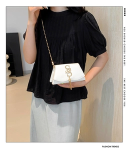 Detail of white leather mini crossbody bag with golden S-logo, tassels, and chain strap