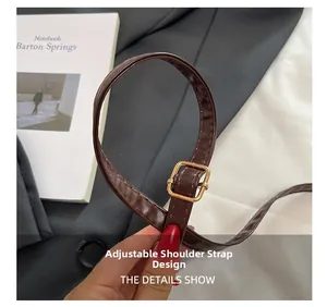 Détail d'une bandoulière en cuir marron foncé réglable avec boucle dorée
