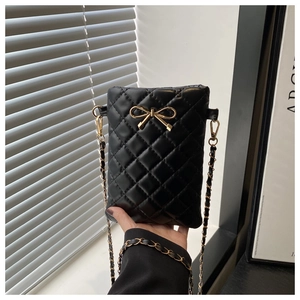Detail of black quilted mini bag featuring a gold bow ornament and metal chain strap