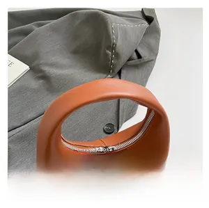 Detail view of orange leather handbag with dual metal zippers and curved handle