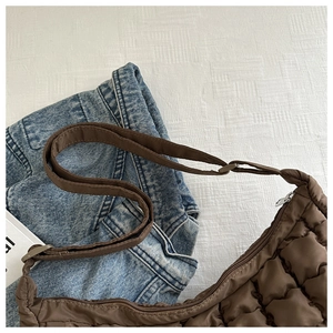 Close-up of brown quilted puffer bag with adjustable strap and silver zipper detail