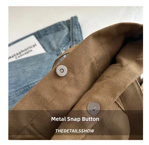 Close-up of the silver magnetic hardware snap on a brown canvas tote bag detail