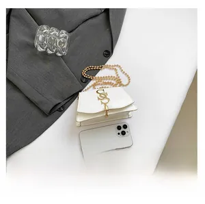White mini crossbody bag with gold S-logo and chain shown next to a phone for scale