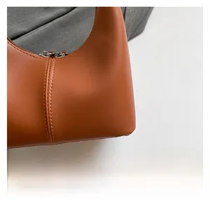 Macro shot of vertical stitching and dual metal zippers on a brown leather handbag