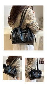 Detail view of glossy black tote bag featuring delicate bow drawstring and sleek texture