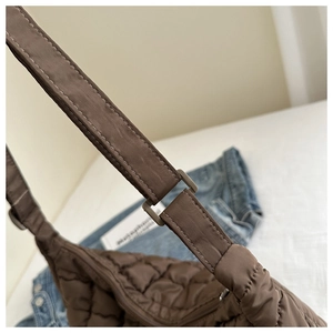 Detailed close-up of brown quilted puffer bag showing nylon texture and adjustable strap buckle