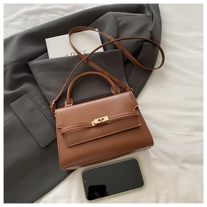 Detail of a brown leather trapezoid handbag with gold hardware on a grey blazer
