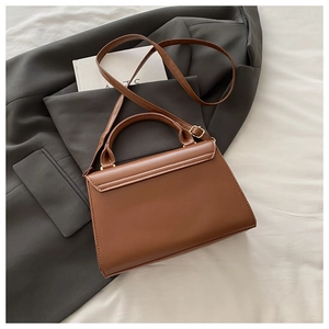 Detailed close-up of brown PU leather shoulder bag with buckle on a fashion backdrop