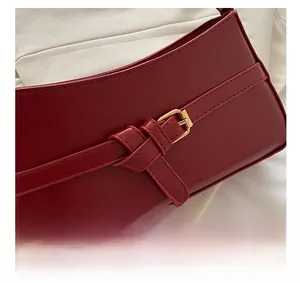 Detail shot of a dark red shoulder bag featuring a smooth leather finish and golden buckle
