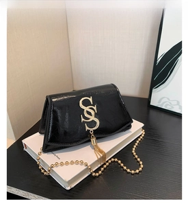 Gros plan d'un sac bandoulière en cuir verni noir avec boucle S dorée et pompon