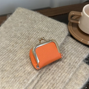 Mini orange litchi grain leather pouch with golden clasp on beige knit background