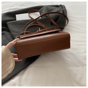 Detail view of the brown leather shoulder bag featuring its base and elegant turn-lock closure