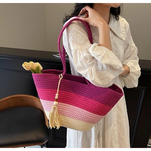 Detail of woven straw tote bag with gradient stripes and decorative tassel charm