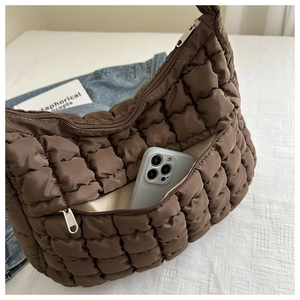 Detail of a brown quilted bubble tote bag with a zipper pocket holding a mobile phone