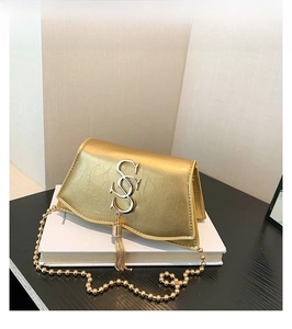 Détail du sac bandoulière en cuir doré avec boucle double S et pompon métallique