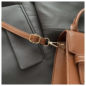 Close-up of golden metal hardware and stitching on a brown leather crossbody bag