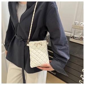 Détail du mini sac blanc matelassé avec nœud doré et bandoulière en chaîne élégante