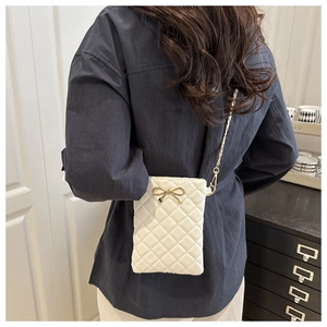 Detail of white quilted crossbody bag with golden bow hardware and chain strap