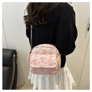 Sac bandoulière en velours côtelé rose avec motifs nœuds porté par un modèle