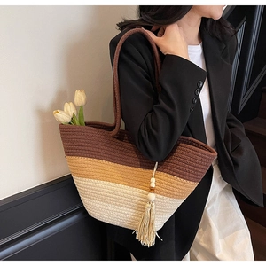 Detailed view of striped woven straw tote bag with beaded tassel and fringe on shoulder
