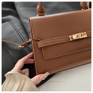 Detailed view of the brown leather texture and golden metal twist lock on the handbag