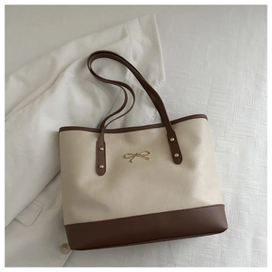 Detail of a minimalist cream tote bag featuring a gold bow accent and brown handles