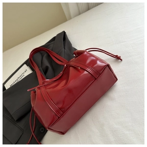 Close-up of wine red patent leather tote bag with drawstring detail on black blazer