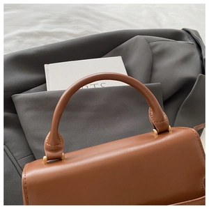 Detail of a brown leather handbag with cylindrical handle and gold metal hardware