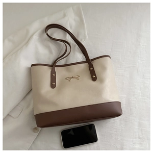 Detail of a beige tote bag with a gold bow metal accent and leather shoulder strap