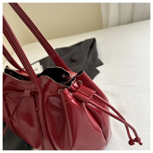 Close-up of red patent leather tote bag with side drawstring and glossy finish detail