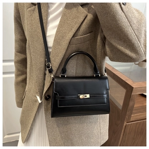 Detail of a black structured leather handbag featuring gold hardware and a top handle