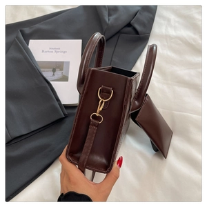 Close-up of dark brown faux leather tote bag with mini pouch and gold hardware on white bedding